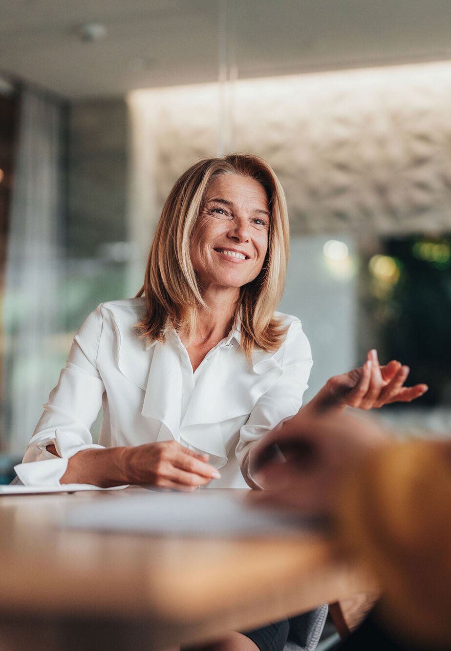 A woman smiling at a desk, in conversation