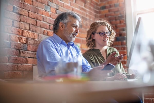 Two people working at a desk with a brick wall behind them
