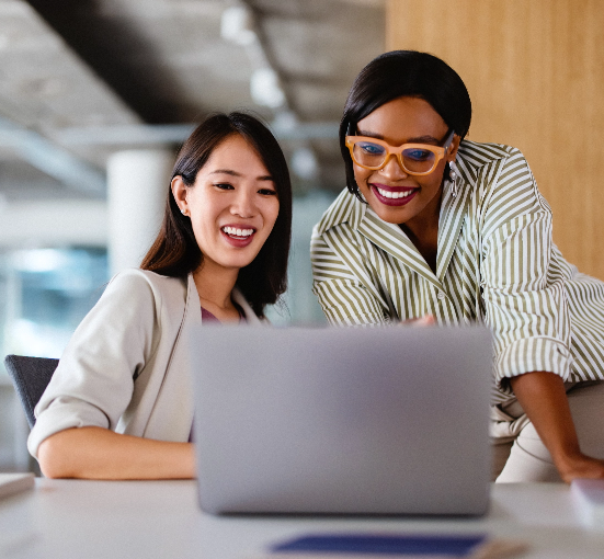 Two women smiling as they review sales data on a laptop