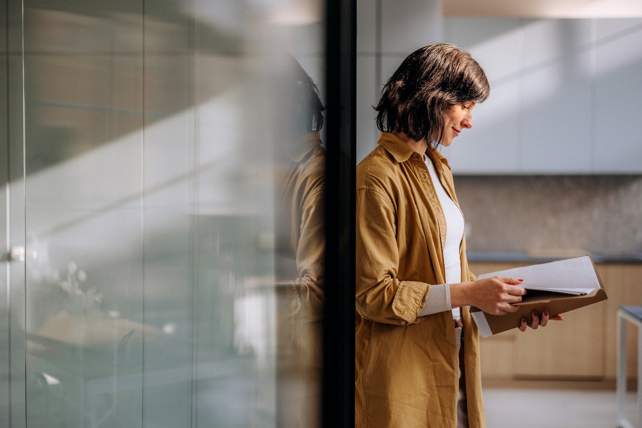 Woman reading papers in a file while she leans against a wall