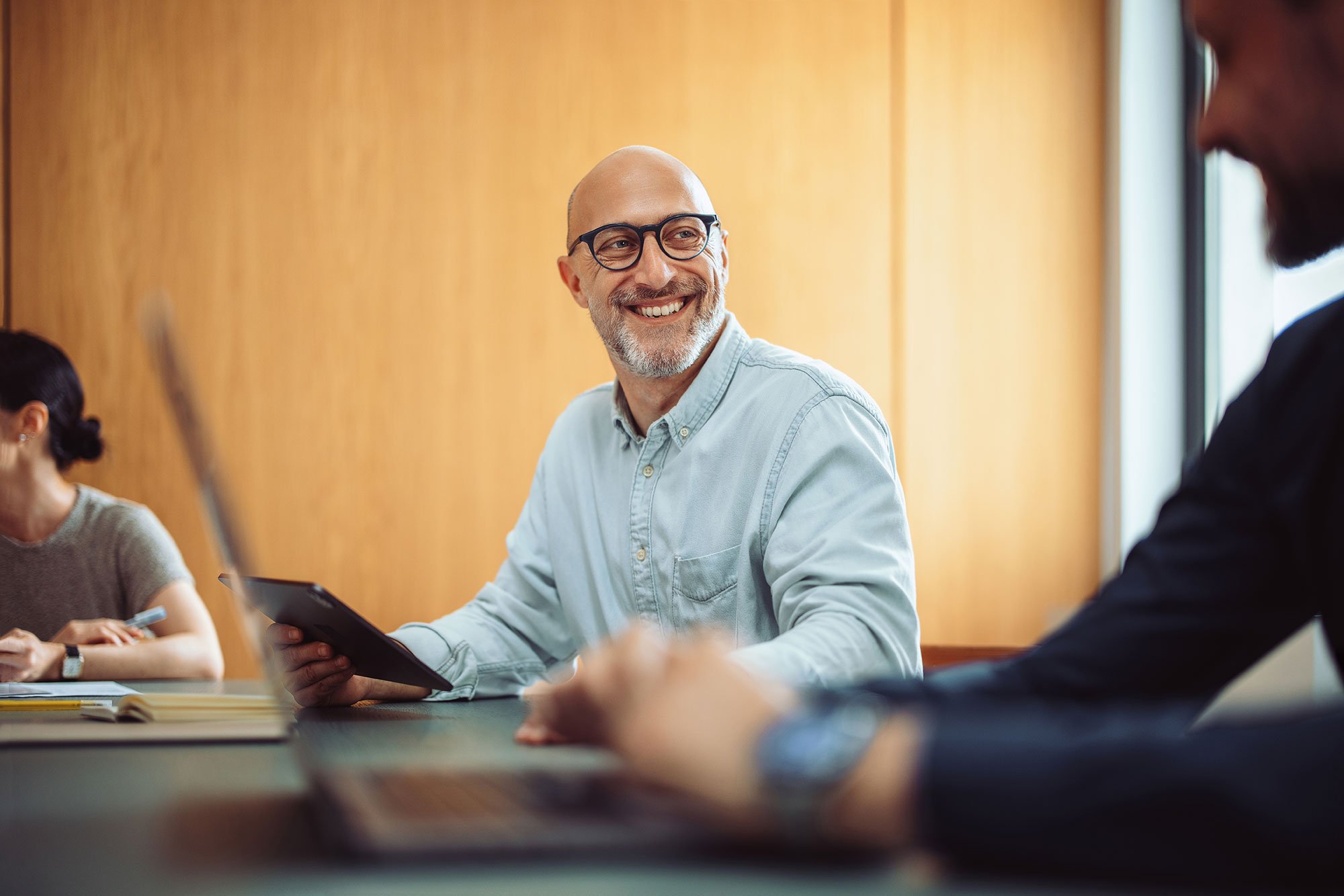 Man with beard and glasses smiling at a conference room desk