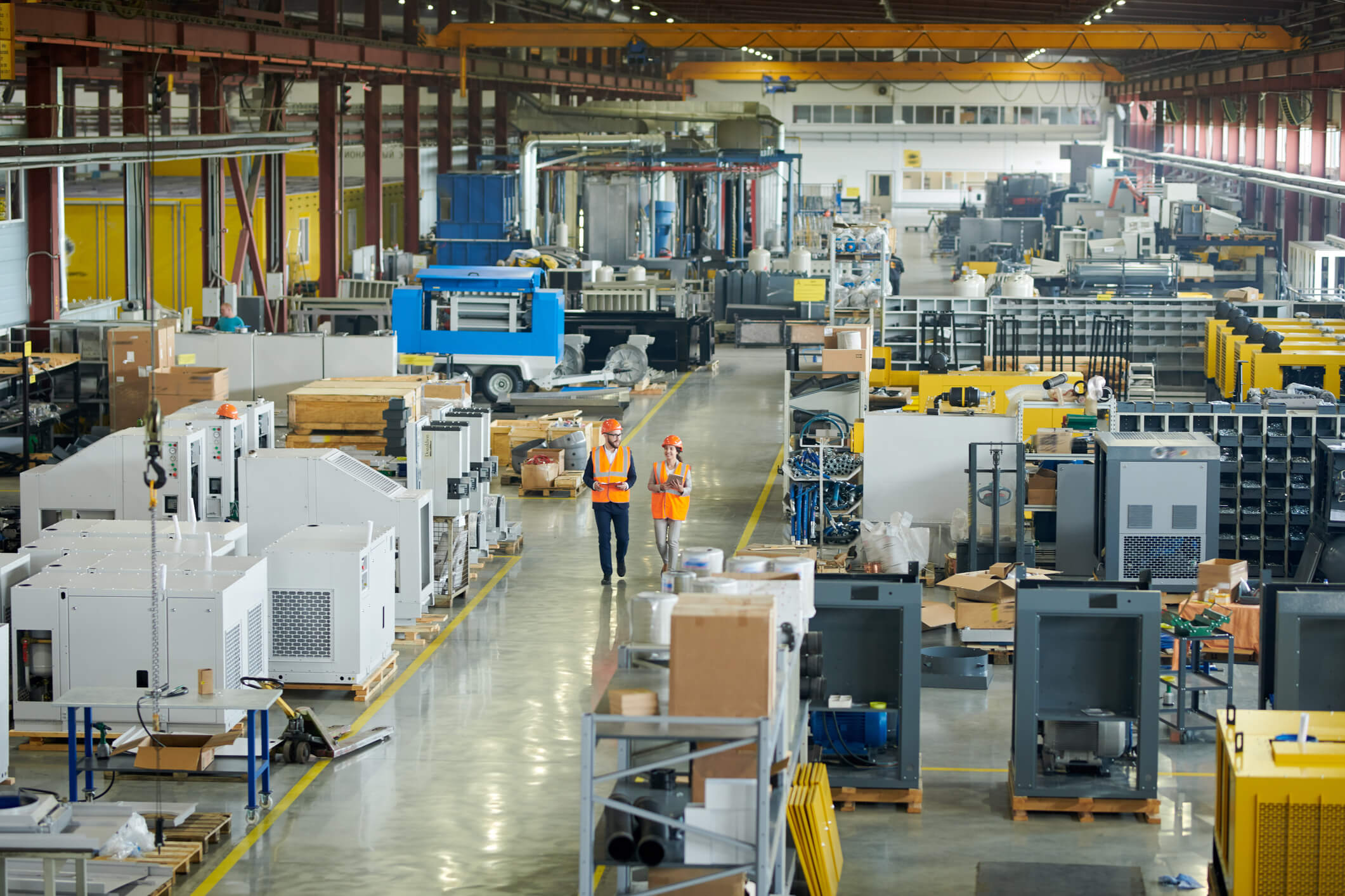 Two people in orange safety vests walking through a manufacturing facility