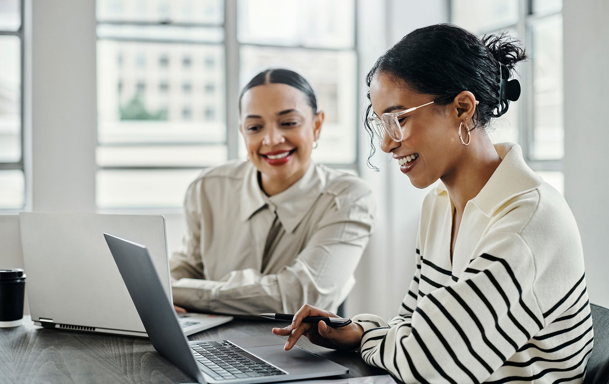 Two woman practicing sales training together using a laptop