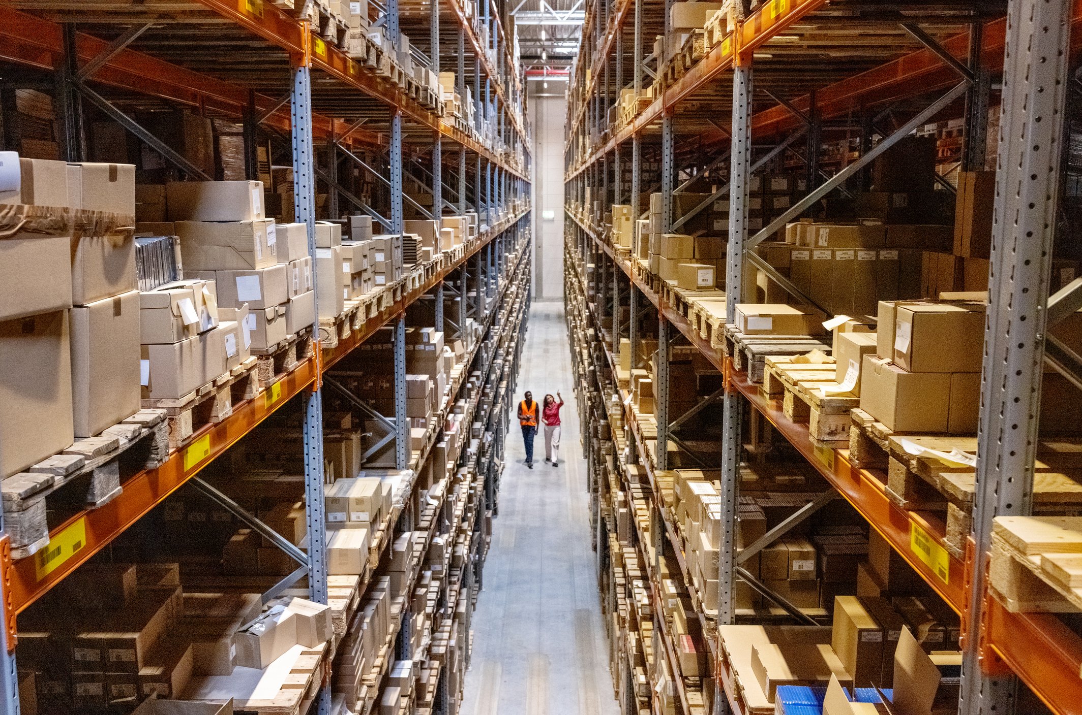 Two people walk between high shelves in a distribution facility